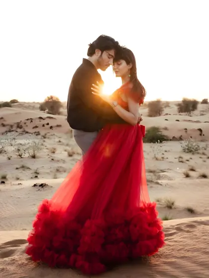 A romantic sunset embrace in the desert. The bold red of the gown creates a stunning visual against the golden sand.