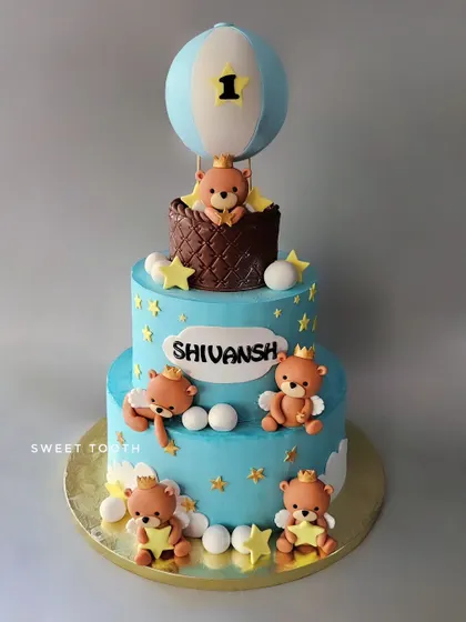A teddy bear themed cake for Shivansh's first birthday. This three-tier cake features cute teddy bears, a hot air balloon, and a beautiful blue color scheme.