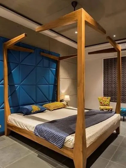 A modern take on a classic four-poster bed. The bold blue geometric headboard adds a pop of color and texture against the concrete-finish wall, creating a look that is both edgy and comfortable.