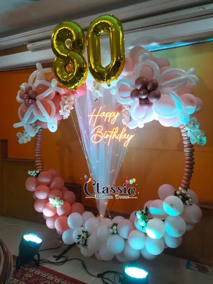 A unique and artistic balloon ring for an 80th birthday, featuring sculpted balloon flowers, tulle fabric, and a neon sign.