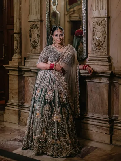 The bride poses confidently in her stunning lehenga, her hand resting on a marble pillar, showcasing the intricate details of her outfit.