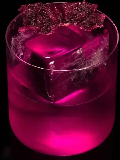 A vibrant magenta cocktail served over a large, clear ice cube. The intense color comes from natural ingredients, creating a visually striking and modern drink.