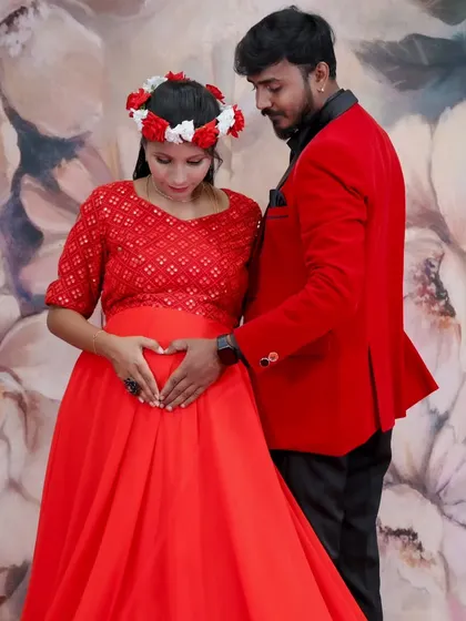 A tender moment between an expecting couple, both dressed in red, making a heart shape with their hands on the baby bump.