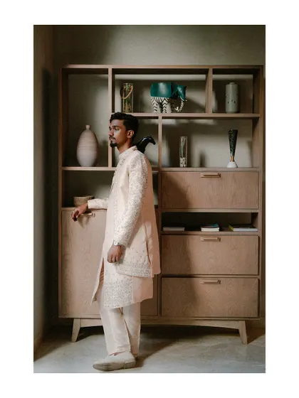 A groom in a beautiful sherwani, captured in a moment of quiet thought. The modern, minimalist decor provides a stylish contrast to his traditional attire.