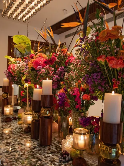 A long view of a tablescape overflowing with colorful flowers and candles. The arrangement, inspired by our work on 'Made in Heaven', uses a rich palette to create a sense of abundance and celebration.