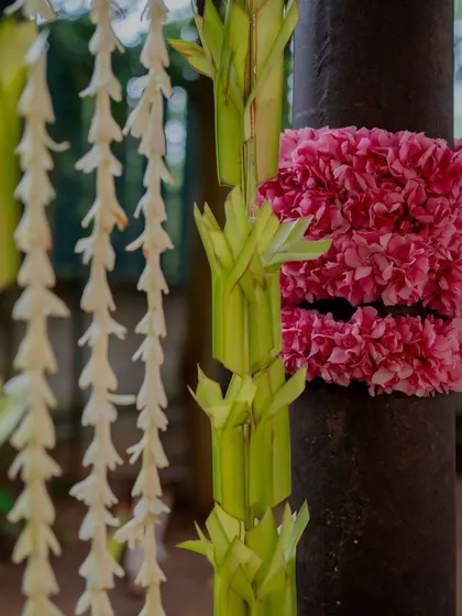 Pillars decorated with pink flowers and woven palm leaves.