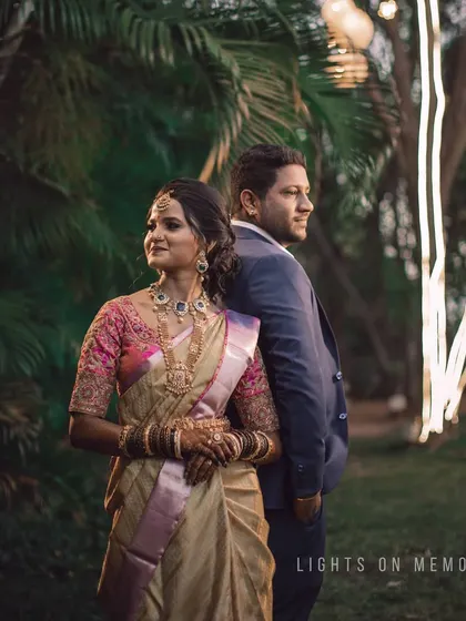 A couple poses back-to-back in a garden setting illuminated by string lights. This creative portrait captures a modern and stylish feel for an evening event.