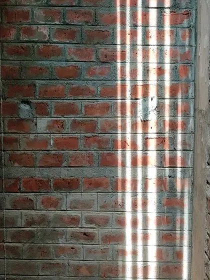 The simple beauty of sunlight casting patterns through a grill onto an unfinished brick wall.
