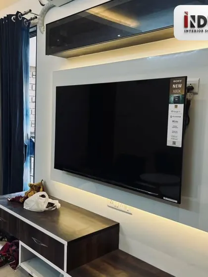 The TV unit is designed with a clean white back panel and ambient backlighting, which reduces eye strain and creates a cinematic feel. The dark wood console offers ample storage.