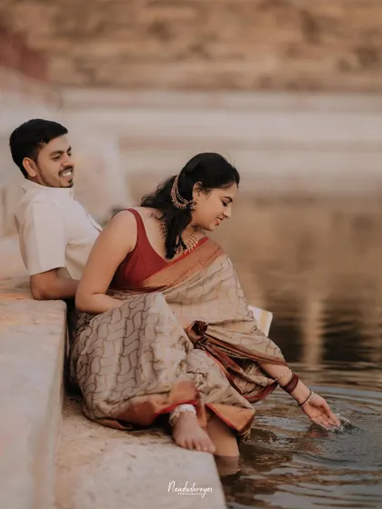 A serene moment of the couple sitting by the temple pond, the bride gently touching the water.