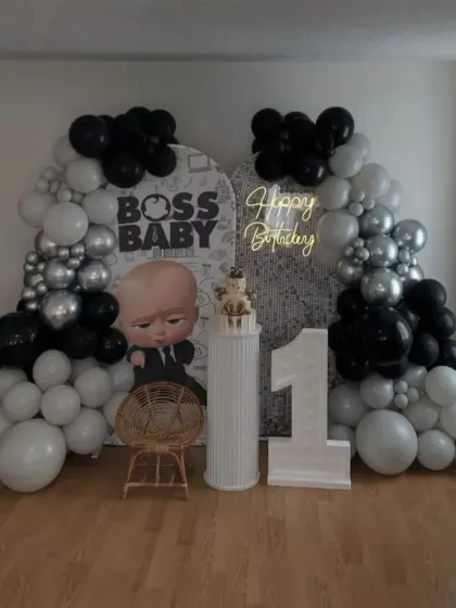 A stylish Boss Baby first birthday in black, white, and silver. The setup includes a custom backdrop, a "1" marquee number, and modern balloon arches.