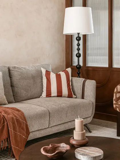 A detail of the living room sofa, styled with a striped rust-colored cushion and a cozy throw. The beaded floor lamp and fluted glass partition in the background add more layers of texture and detail.