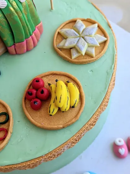 More miniature food toppers for the baby shower cake, including plates of kaju katli, bananas, and apples. Each tiny piece is sculpted by hand.