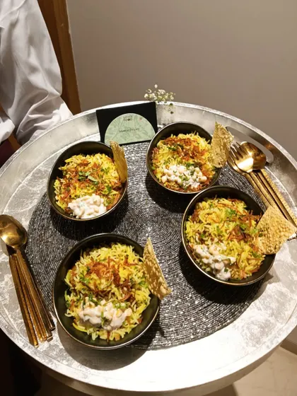A server holding a tray of individual biryani bowls. This is a modern way to serve a classic Indian dish, making it easy for guests to enjoy while standing and mingling at an event.
