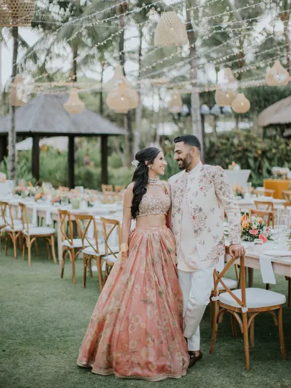 Posing by their beautiful outdoor sangeet setup. The soft peach and floral theme of their outfits ties in perfectly with the event's decor, creating a cohesive and visually stunning aesthetic.