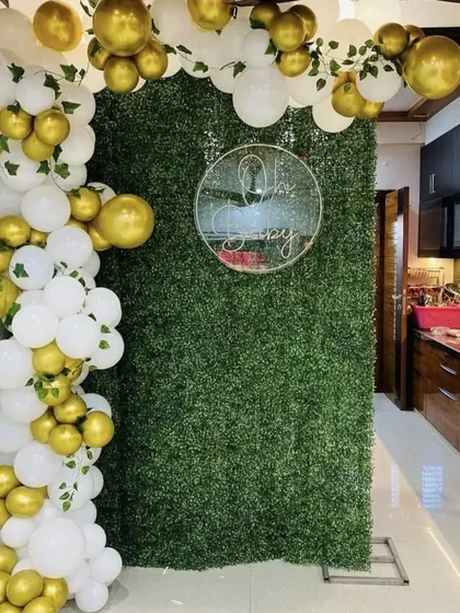 An elegant baby shower backdrop using a lush green foliage wall. The white and gold balloon garland with ivy accents creates a fresh and sophisticated look.