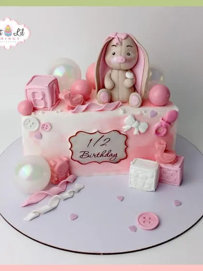 A sweet half-birthday cake in shades of pink. This design features a cute bunny, baby blocks, and pearlescent bubble decorations.