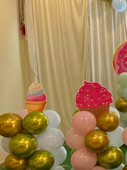 A close-up of candyland party decorations, showing cupcake and ice cream cutouts on top of balloon clusters.