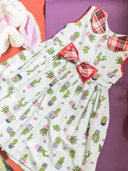 A flat-lay of the cactus print dress, showing off the fun pattern and cute details like the plaid bow and collar.