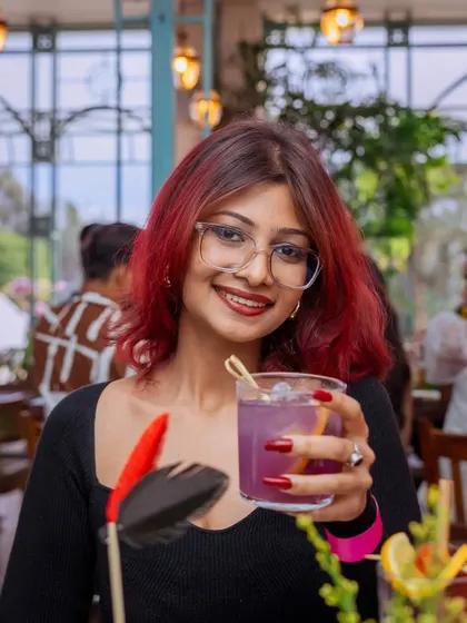 A guest with vibrant hair holds a colorful cocktail, perfectly matching the lively atmosphere of my mansion. Here, every detail, from the drinks to the decor, is part of the story.