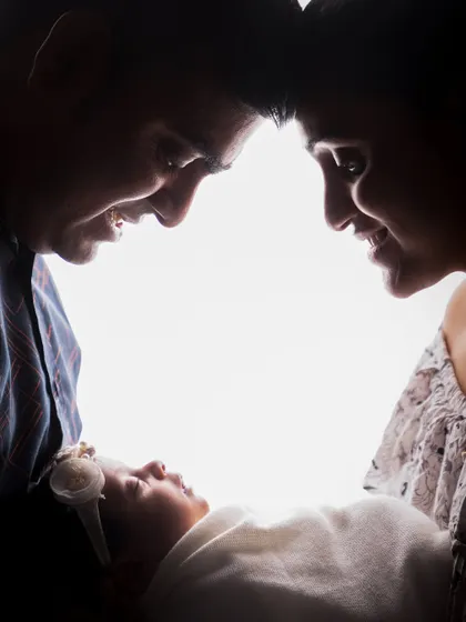 An intimate close-up of a family silhouette, focusing on the loving expressions of the parents as they admire their newborn. The bright backlighting creates a halo effect, symbolizing their new world.