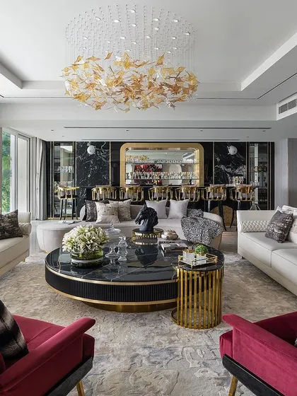 A luxurious living room where we provided custom furniture. The space features white sofas, bold red armchairs, and a statement black and gold coffee table, all unified by a stunning leaf-motif chandelier. This demonstrates how our bespoke furniture can transform a space.