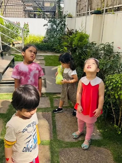 Children look up at the sky and around the garden, observing how the sun's position affects the shadows of trees and buildings. This is a simple, powerful lesson in earth science.