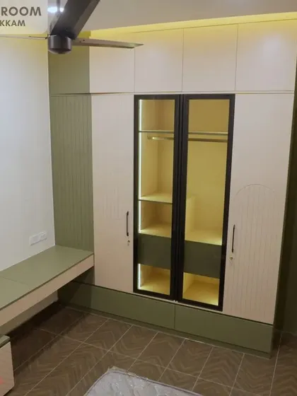 Another daughter's bedroom in the Ayyapakkam villa, with a light green and cream wardrobe that includes an illuminated glass display section and an integrated study desk.
