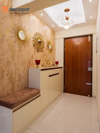 This foyer design exudes warmth and glamour, with a textured gold wallpaper and decorative sunburst mirrors. The off-white shoe cabinet includes a comfortable brown seater for convenience.