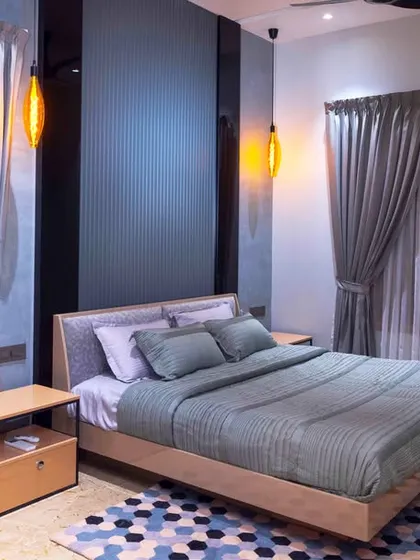 A modern bedroom with a dramatic dark blue accent wall and floor-to-ceiling curtains. The simple wooden bed frame and geometric rug complete the stylish and contemporary look.