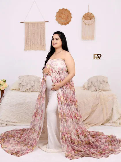 This unique gown features a floral overlay on top of white pants, offering a modern and stylish alternative to traditional maternity dresses. It's perfect for a chic, boho-inspired look.