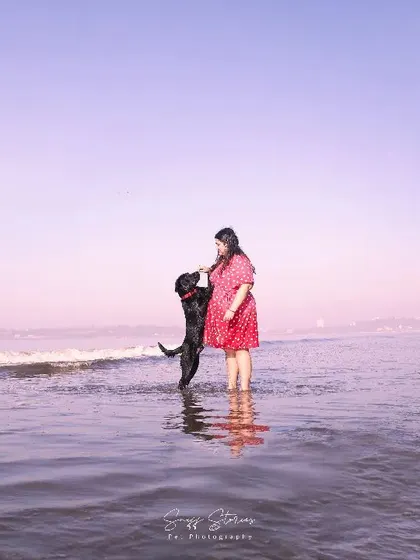 The world fades away when it is just you and your best friend. This wide shot captures the beautiful solitude and connection between a pet parent and her dog, standing together in the calm ocean water against a soft, pastel sky.