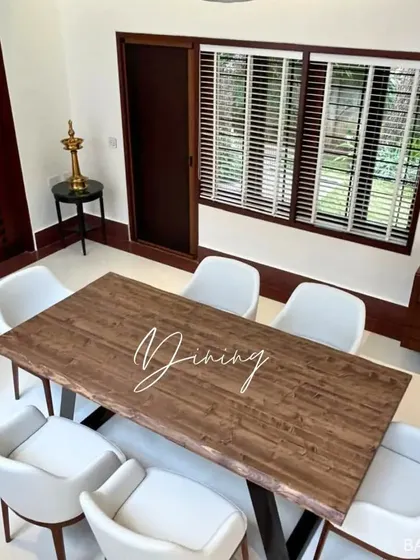 A dining area that blends rustic and modern styles, with a live-edge wood table, contemporary white chairs, and dark wood window frames.