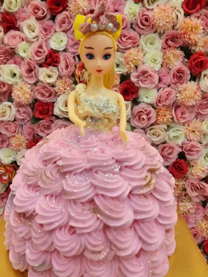 This doll cake features a pink ruffled dress made of buttercream, with a touch of glitter for extra sparkle. It's a princess-perfect cake for a special day.