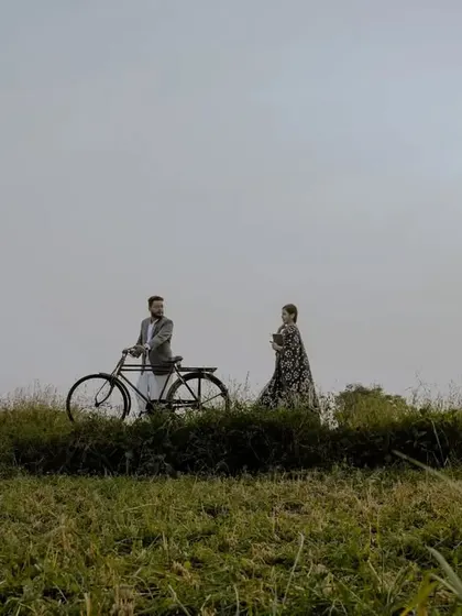A scenic, wide-angle shot of the couple with their bicycle against the setting sun, creating a beautiful silhouette effect.