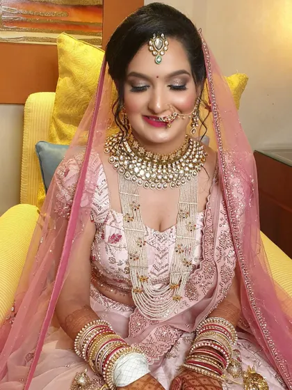 A lovely shot of the bride seated, showcasing her complete look. The intricate pearl and kundan jewellery beautifully complements the delicate embroidery on her pastel pink lehenga.
