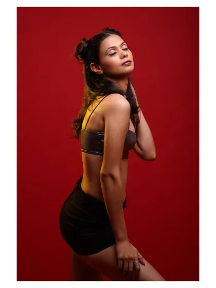 A fun and edgy studio portrait with a red background. The model's pose is playful and confident.