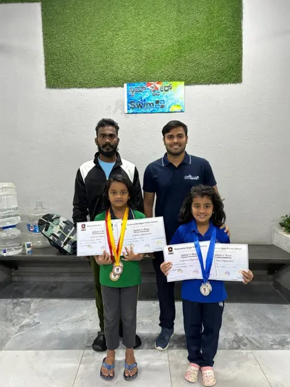 Two of our youngest female swimmers with their coaches, proudly holding their medals and certificates from the Splash N' Dash competition.