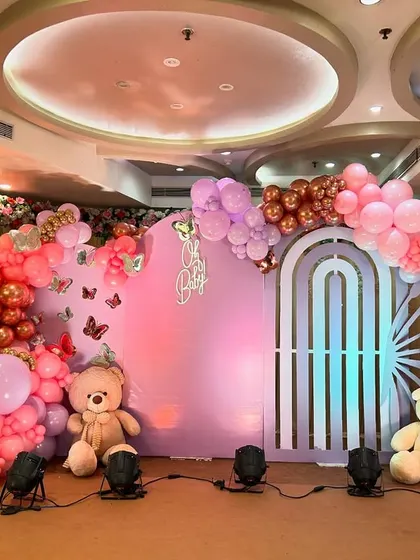A grand 'Oh Baby' shower with a butterfly theme. This stage features a large pastel purple backdrop, butterfly wing-shaped balloon arrangements, and cute teddy bears for a whimsical touch.
