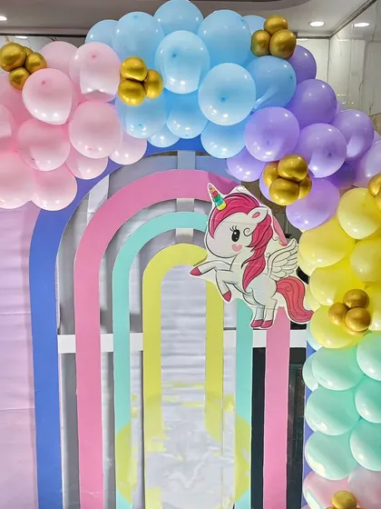 A rainbow-striped archway decorated with pastel balloon's and a unicorn cutout.