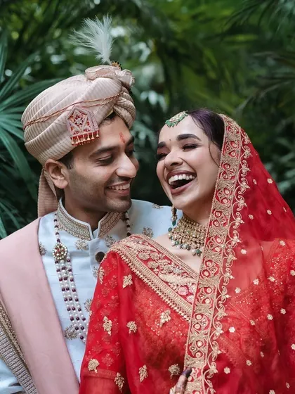 A candid portrait of a couple sharing a laugh, dressed in beautiful red and white traditional wedding attire.