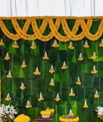 A backdrop of fresh banana leaves decorated with garlands of marigold and jasmine, creating a natural and traditional look for a Haldi ceremony.
