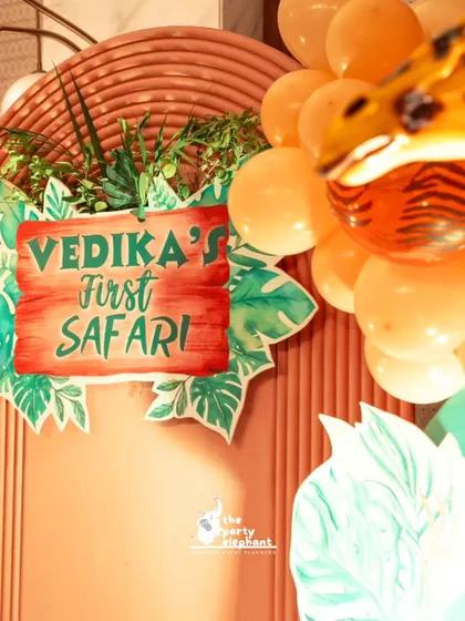 A close-up of the custom 'Vedika's First Safari' sign, designed with a wooden texture and surrounded by tropical leaves to perfectly match the jungle theme.