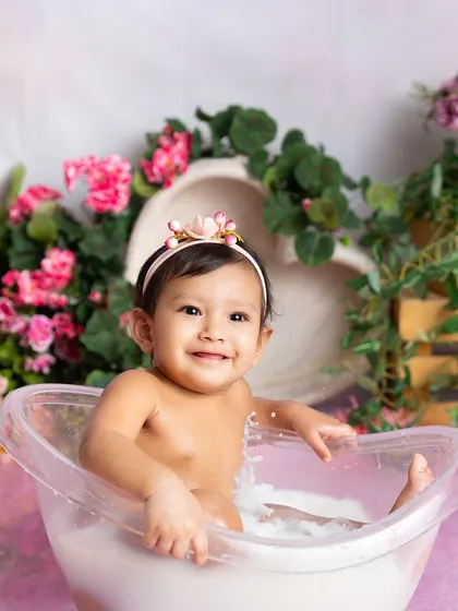 A gentle splash and a sweet smile. This baby is thoroughly enjoying her warm milk bath surrounded by beautiful pink flowers.