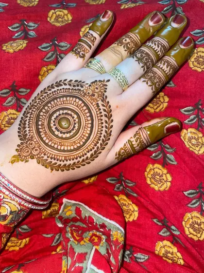 A classic mandala design with a leafy border, shown here with fresh henna paste. The details on the fingers complement the central pattern perfectly.