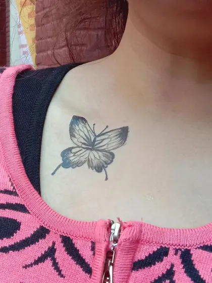A classic black and grey butterfly temporary tattoo on the collarbone. It has the detailed look of a real tattoo.
