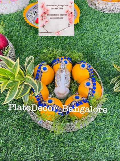 A basket of oranges decorated with blue fabric and kundan stones, with a silver swan figurine placed in the middle.