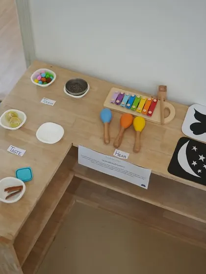 This is one of our learning stations, carefully set up with sensory materials. It includes items for exploring taste, sound with a xylophone, and sight with high-contrast cards for our youngest learners.