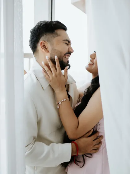 A moment of pure, uninhibited laughter between a couple. This candid shot, framed by soft curtains, captures the playful and joyful side of their relationship perfectly.