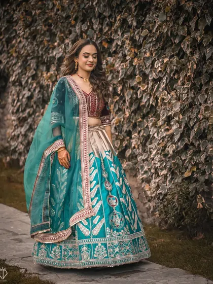 A full-length shot of the bride-to-be in her gorgeous turquoise and maroon lehenga, walking along a path lined with ivy.